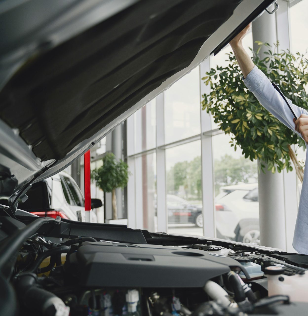 Ein Mann, der sorgfältig einen Automotor in einem hellen, modernen Autohaus überprüft.
